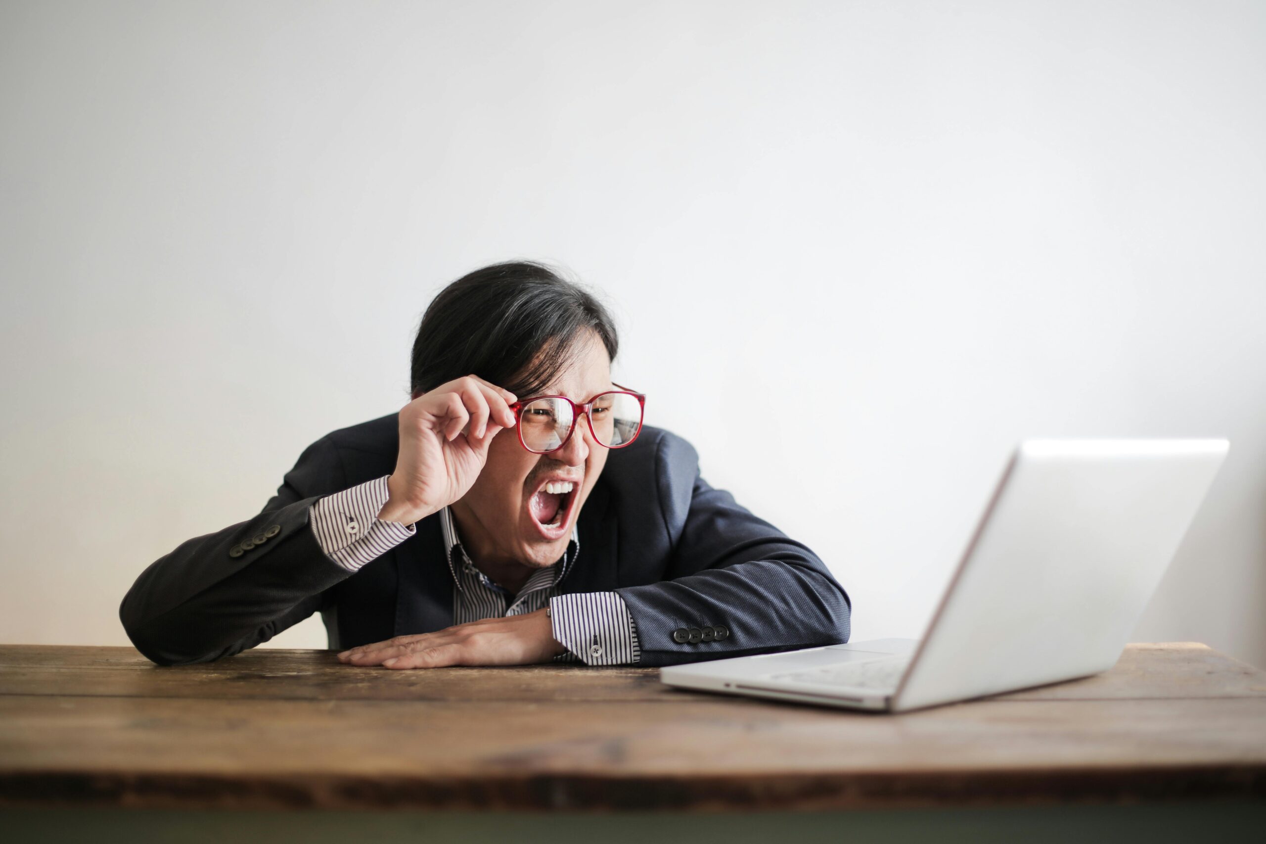 man zit achter zijn bureau en schreeuwt uit frustratie naar zijn laptop